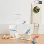 Preview: Rosa und hellblaue Miniatur-Strickmützen mit weißen Bommeln neben Miniatur-Strickzeug in einer Wichteltür-Szene