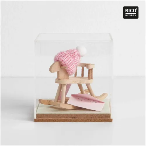 Rosa Miniatur-Strickmütze mit weißer Bommel auf einem Mini-Schaukelpferd unter einer Glashaube als liebevoll gestaltete Geschenkdekoration