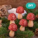 Holzpilze mit irisierendem Glitter und kleinen Tannenzweigen auf einer Holzscheibe als dekoratives Arrangement gestaltet